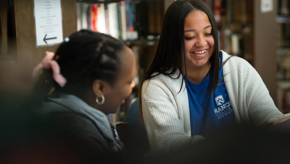 Manor College practical nursing student smiling while studying with a classmate in the campus library.