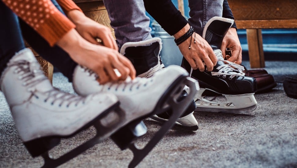 Young couple preparing to a skating. Close-up photo of their hands tying shoelaces of ice hockey skates in a locker room.