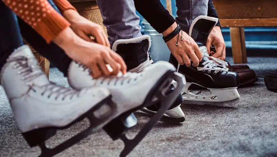 Young couple preparing to a skating. Close-up photo of their hands tying shoelaces of ice hockey skates in a locker room.