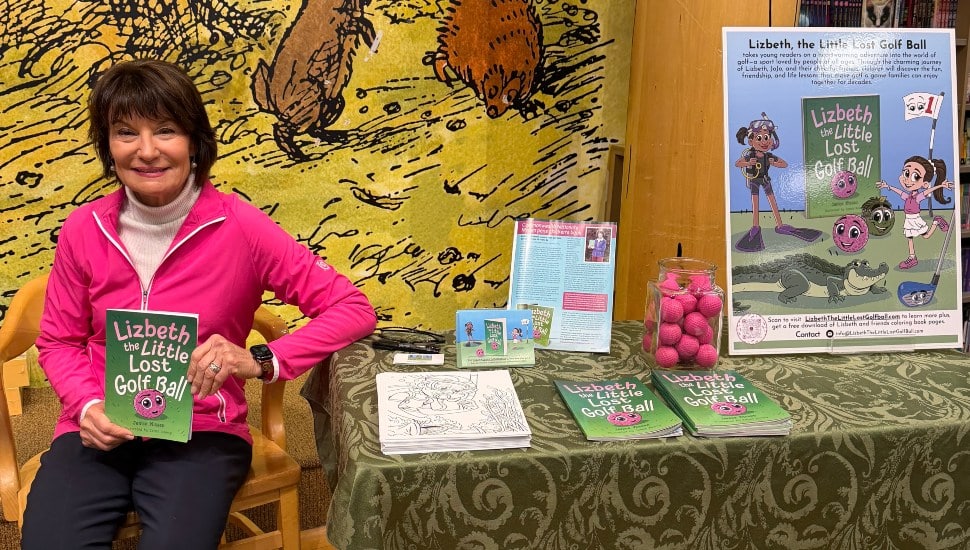 Janice Nissen sits next to a table as she signs copies of her book, Lizbeth, the Little Lost Golf Ball.