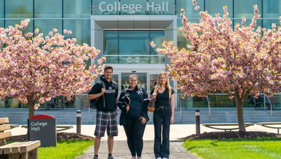 Students walking outside College Hall on Montgomery County Community College’s Blue Bell campus, framed by blooming cherry blossom trees.