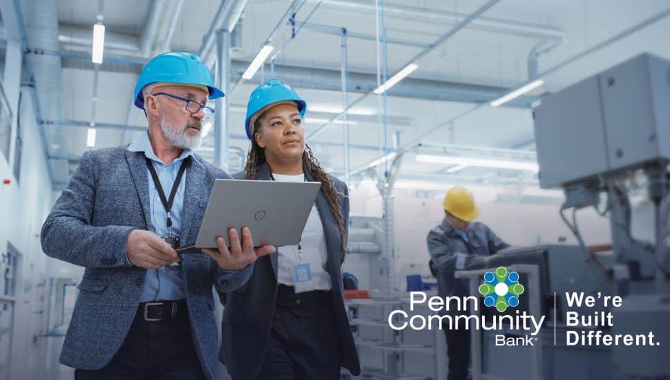 Penn Community Bank advisors review digital payment operations with a business owner inside a modern manufacturing facility.