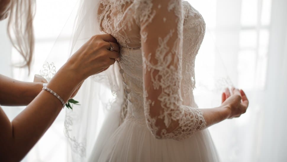 Bridesmaid making a bow-knot on the back of brides dress/