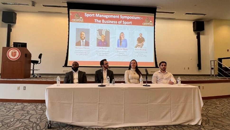 Four panelists sit at table for symposium.