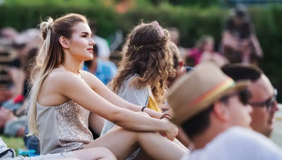 Two women sit in the grass at an outdoor concert.