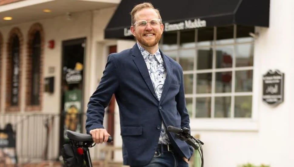 A sharply-dressed Ross Abel stands outside with his bike.