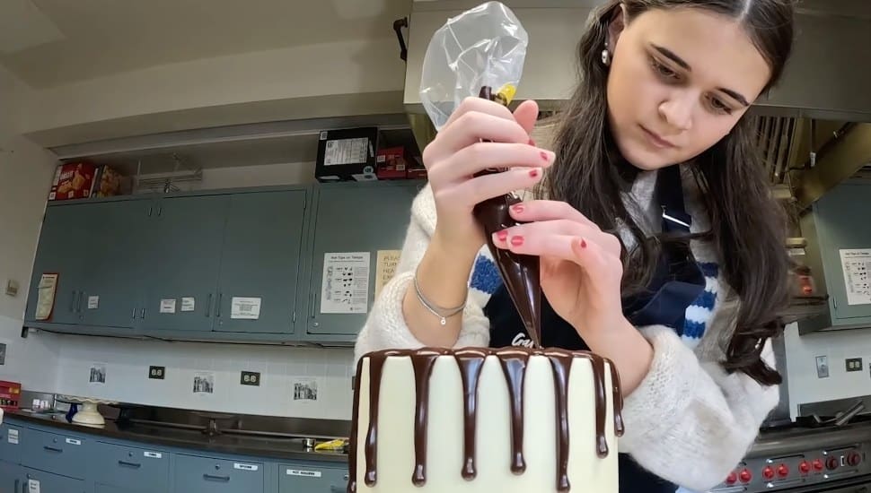 Sarah Kokas pours chocolate frosting on a cake.