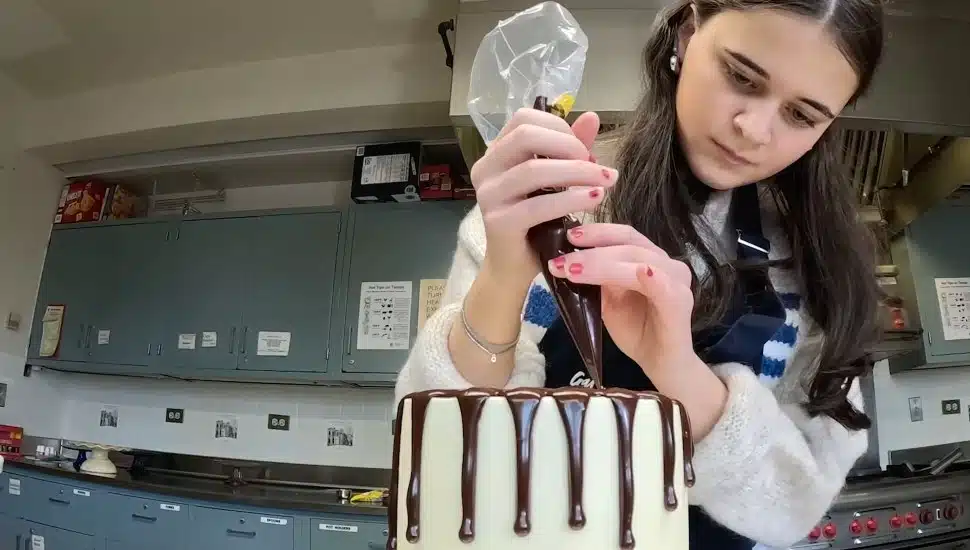 Sarah Kokas pours chocolate frosting on a cake.