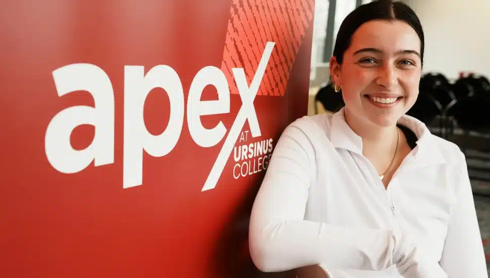 An Ursinus student smiles next to an APEX sign.