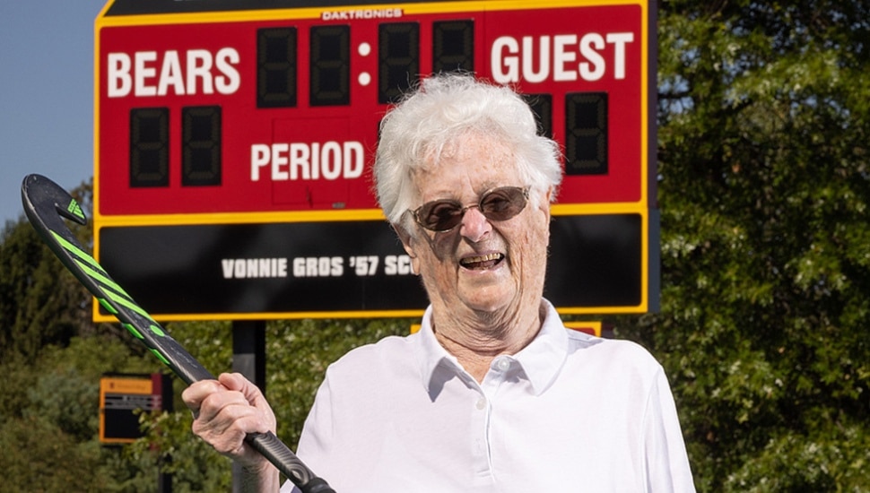 Vonnie Gros holds a field hockey stick in front of an Ursinus College scoreboard.