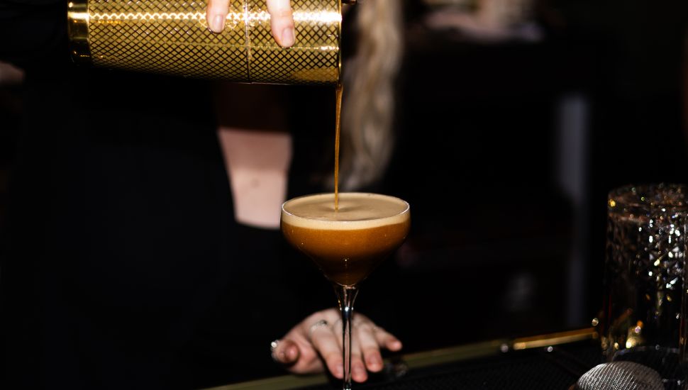 Perfectly Crafted Espresso Martini - Expert Mixology. close up image of drink being poured at bar.