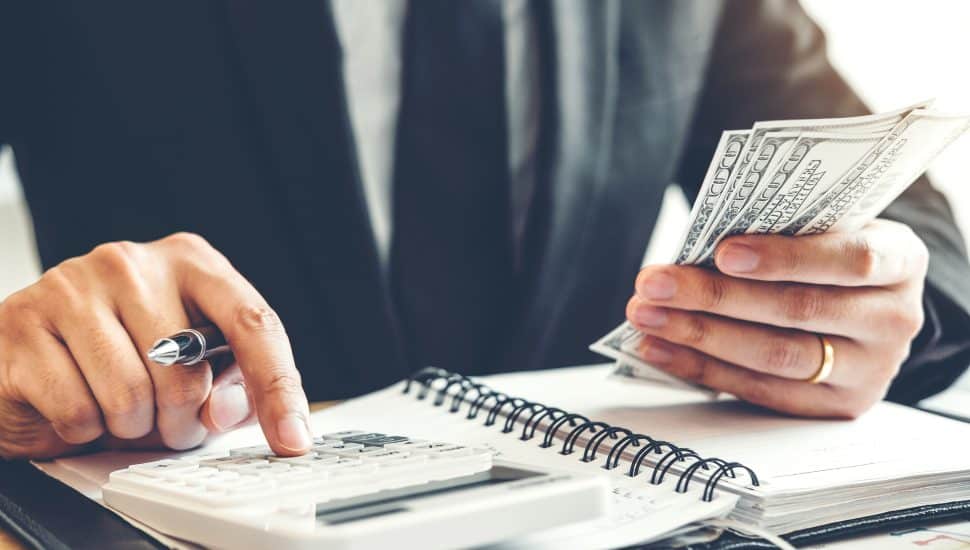 Businessman uses calculator with money in hand.