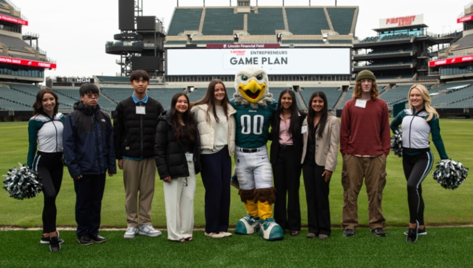 Students and Eagles mascot and cheerleaders pose for picture in football stadium.