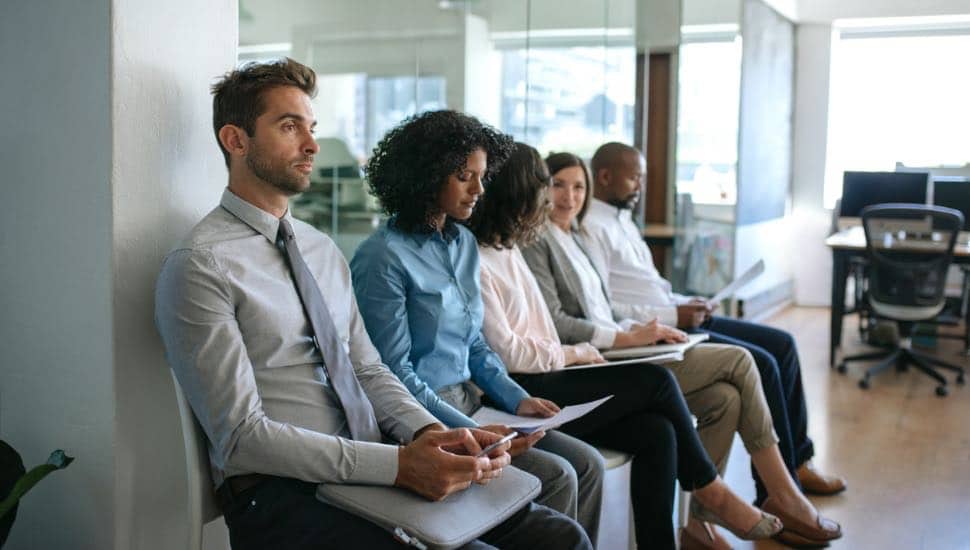 Diverse group of job applicants sitting together outside of an office waiting to be interviewed.
