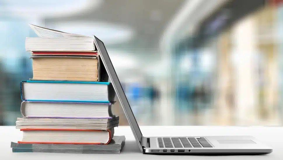 Stack of books with laptop on wooden table.