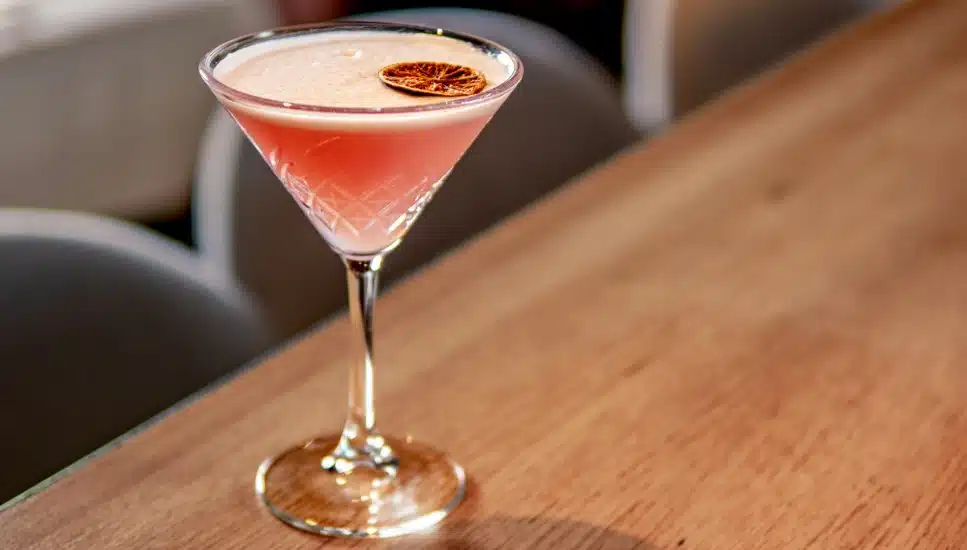 Red cocktail in martini glass on bar counter in restaurant interior.