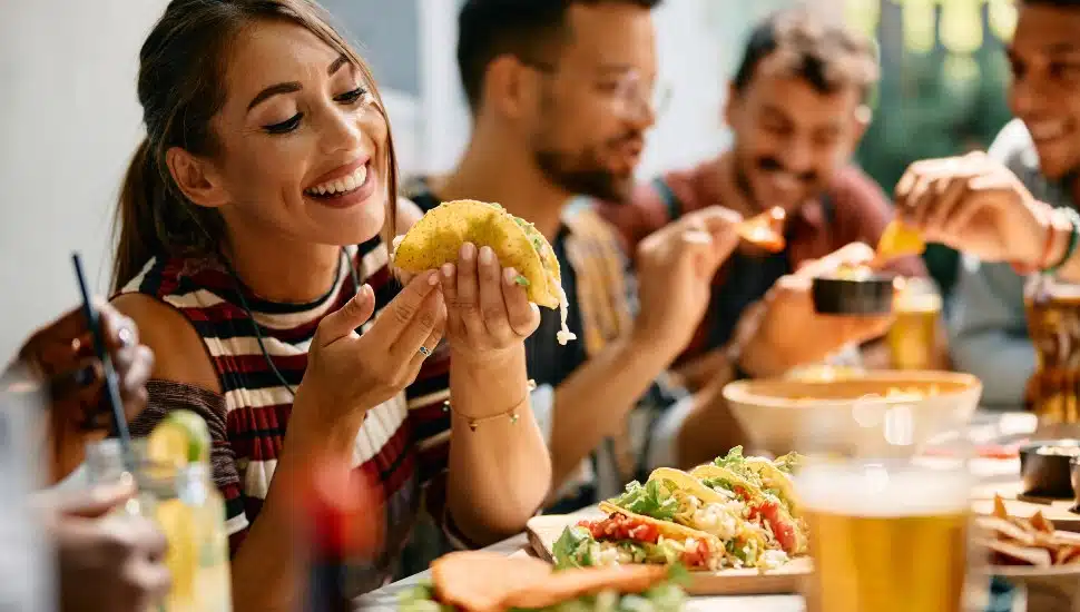 Young woman enjoying in a taste of tacos while having lunch with friends in restaurant.
