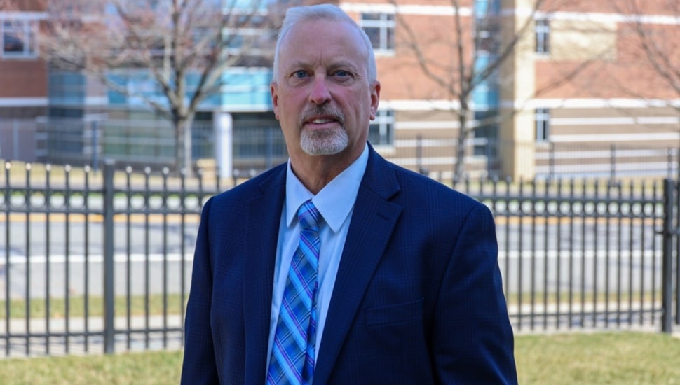 Middle-aged man poses for picture on college campus.