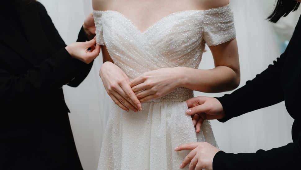 Helpers adjust bride dress at fitting in salon.