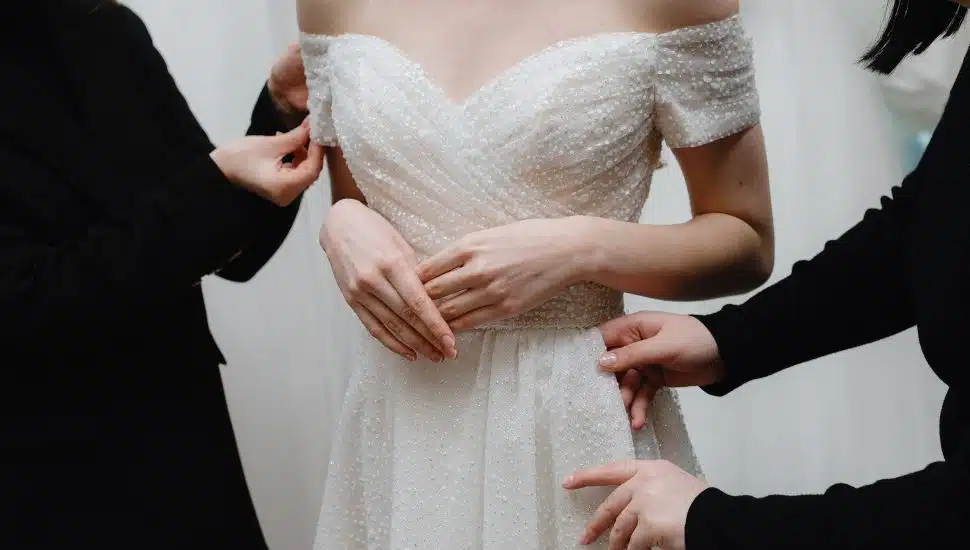 Helpers adjust bride dress at fitting in salon.