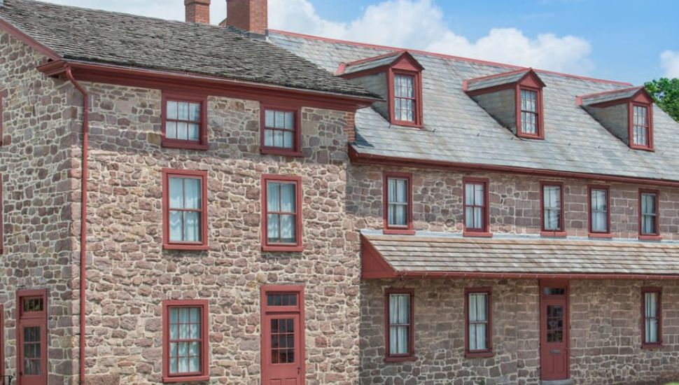 Historic stone building in Trappe, Pennsylvania with red-trimmed windows and doors, part of the Muhlenberg family historic site under a blue sky.