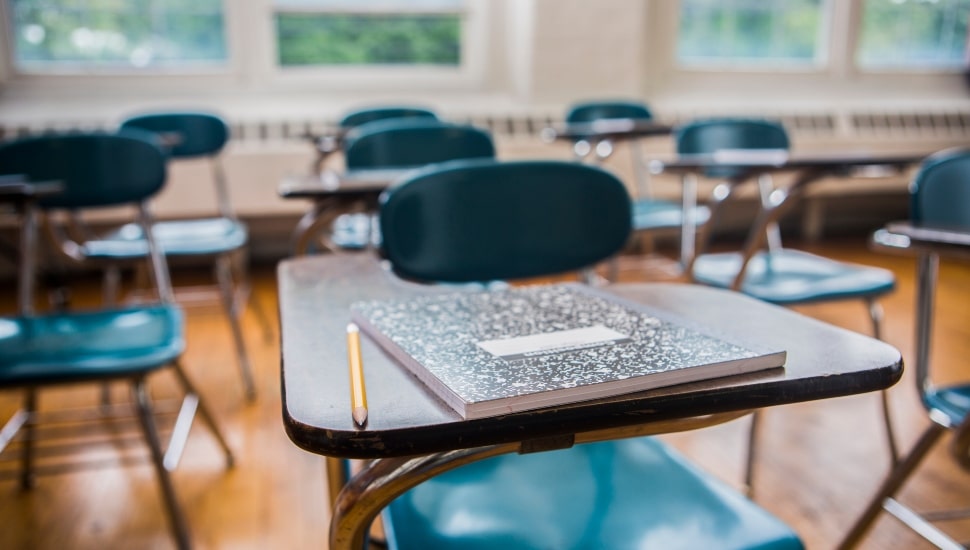 A notebook and pencil on a desk in a school classroom.