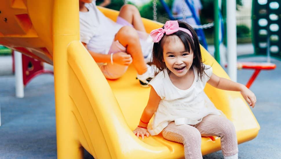 Kids sliding downs a slide at a playground.