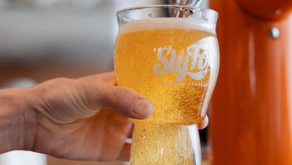 A hand fills a Sly Fox beer glass with beer from a tap.