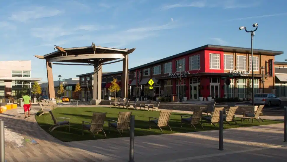 King of Prussia Town Center featuring outdoor seating, open green space, retail storefronts, and pedestrian walkways under a clear blue sky.