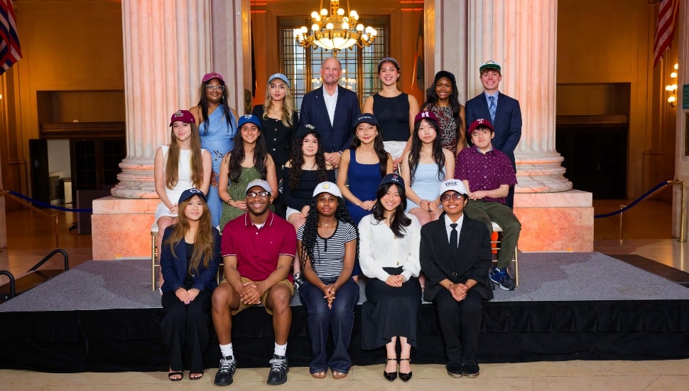 Scholarship recipients wearing hats of their college choice pose for group photo with bank executive.