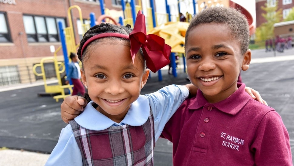 Young boy and girl smile for picture on playground at a Catholic school.