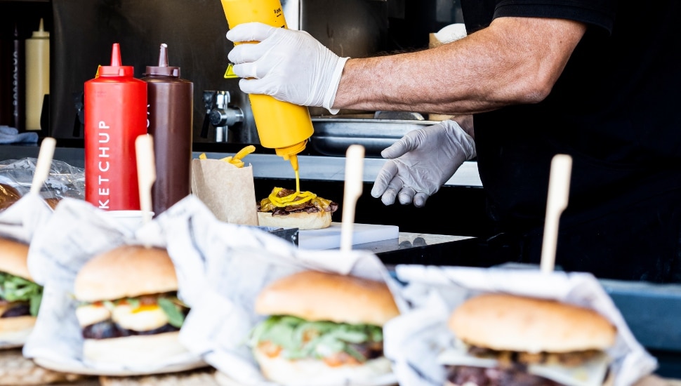 A man in a food truck adds condiments to a burger.
