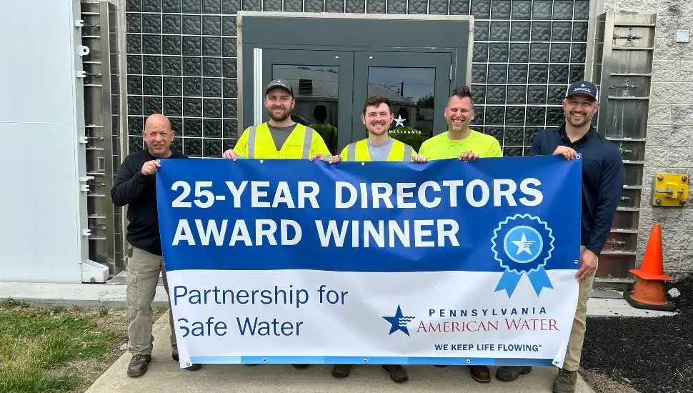 Five Pennsylvania American Water employees stand outside the Norristown Water Treatment Plant holding a banner celebrating the facility's 25-Year Directors Award from the Partnership for Safe Water.