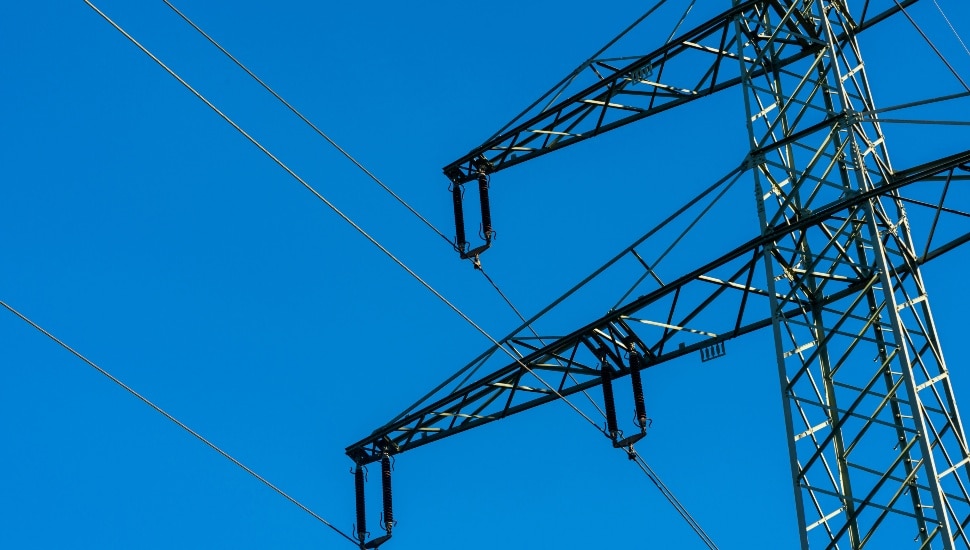 Close-up of a high-voltage transmission tower, electricity pylon, against a clear blue sky. The metal structure of the tower is prominently displayed.