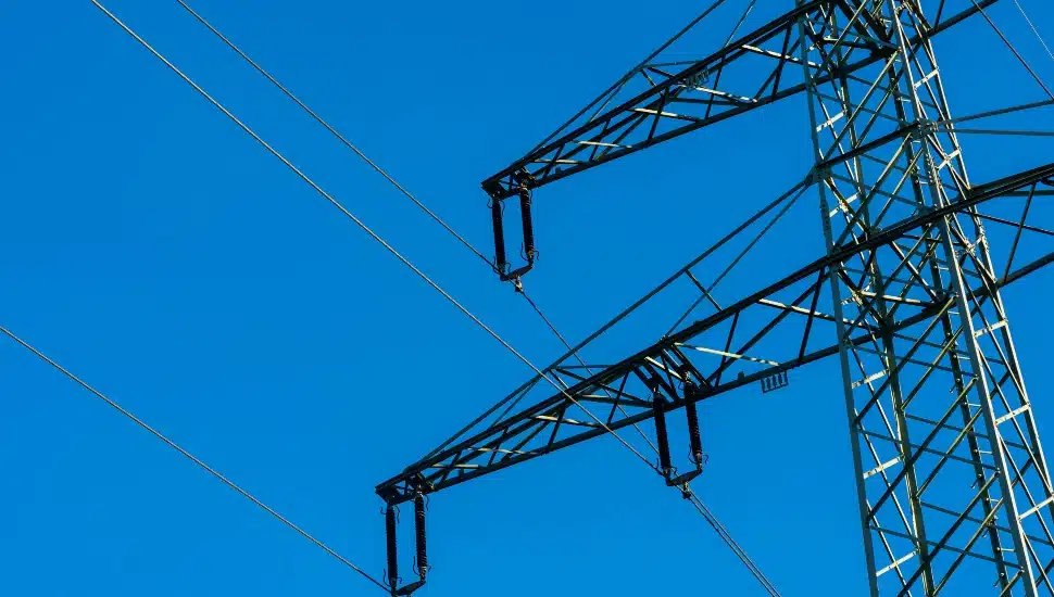 Close-up of a high-voltage transmission tower, electricity pylon, against a clear blue sky. The metal structure of the tower is prominently displayed.