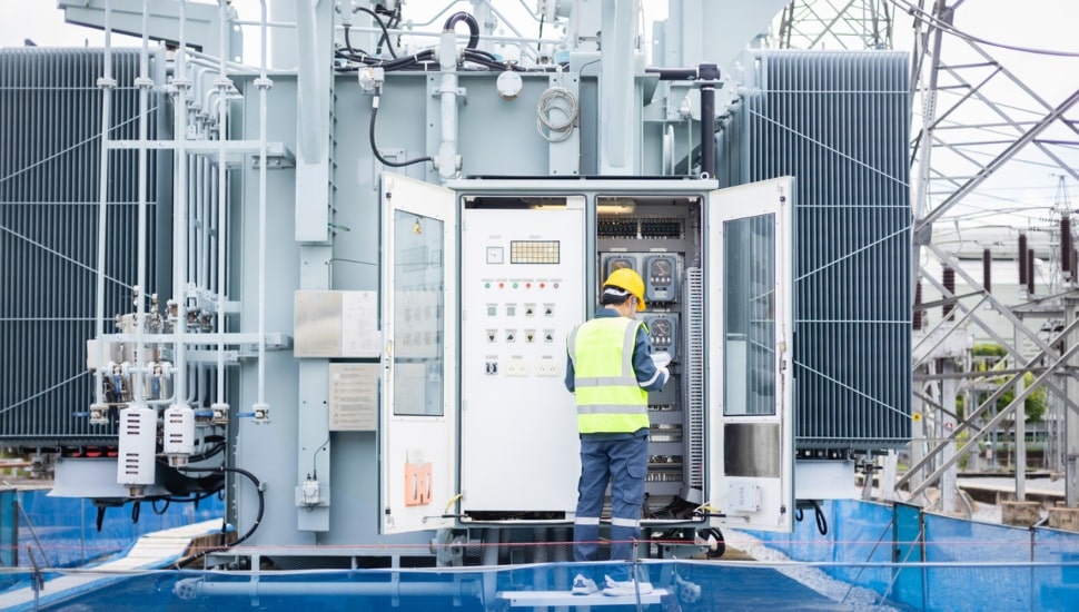 An engineer is working on high voltage power substation performing inspection and check to ensure infrastructure operates safely and efficiently in this industrial environment