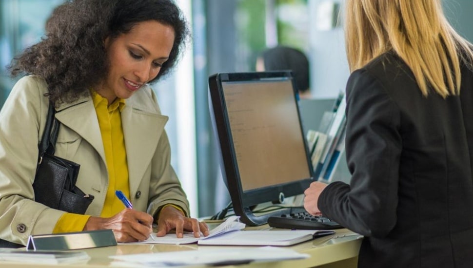 Woman signs check for deposit with bank teller.