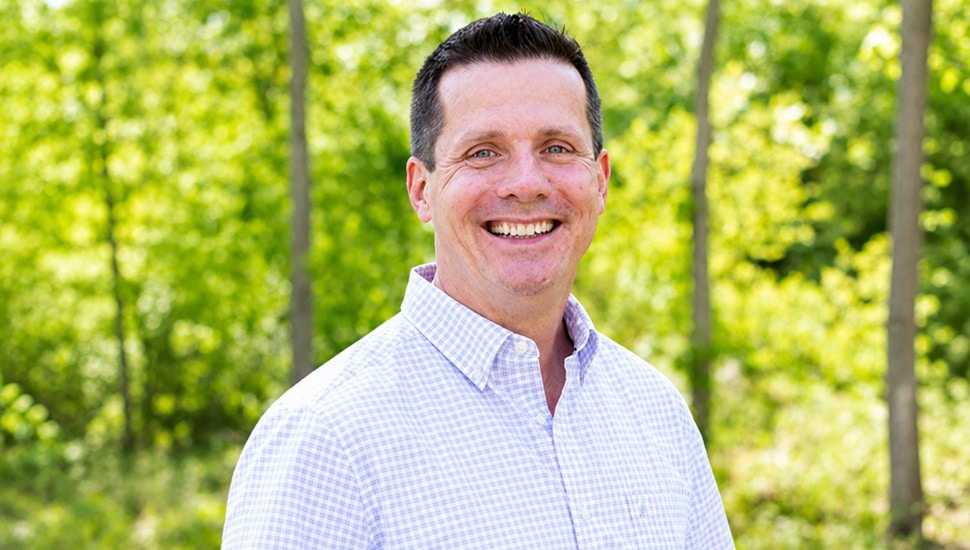 Headshot of middle-aged man with green forest in background.