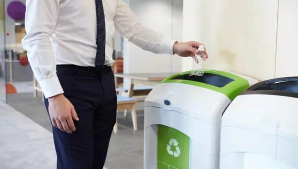 close up of man putting bottle in recycle bin in office.