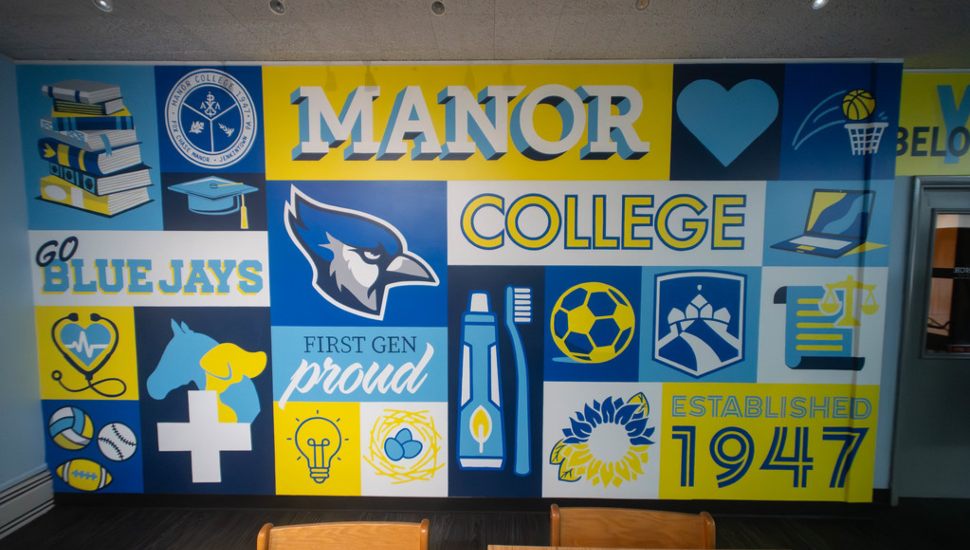 A colorful mural inside Manor College featuring the Blue Jays mascot, academic and athletic symbols, books, graduation imagery, healthcare and technology icons, and messages celebrating student success, school pride and the college's founding in 1947.