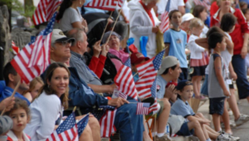 Families lining the parade route at a Fourth of July celebration in Montgomery County, Pennsylvania, waving American flags as the procession passes by.